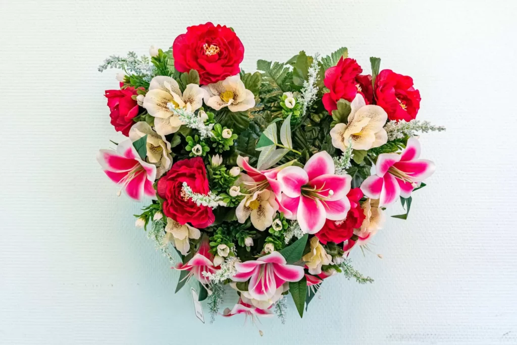 Couronne funéraire en forme de cœur composée de fleurs rouges, roses et blanches.